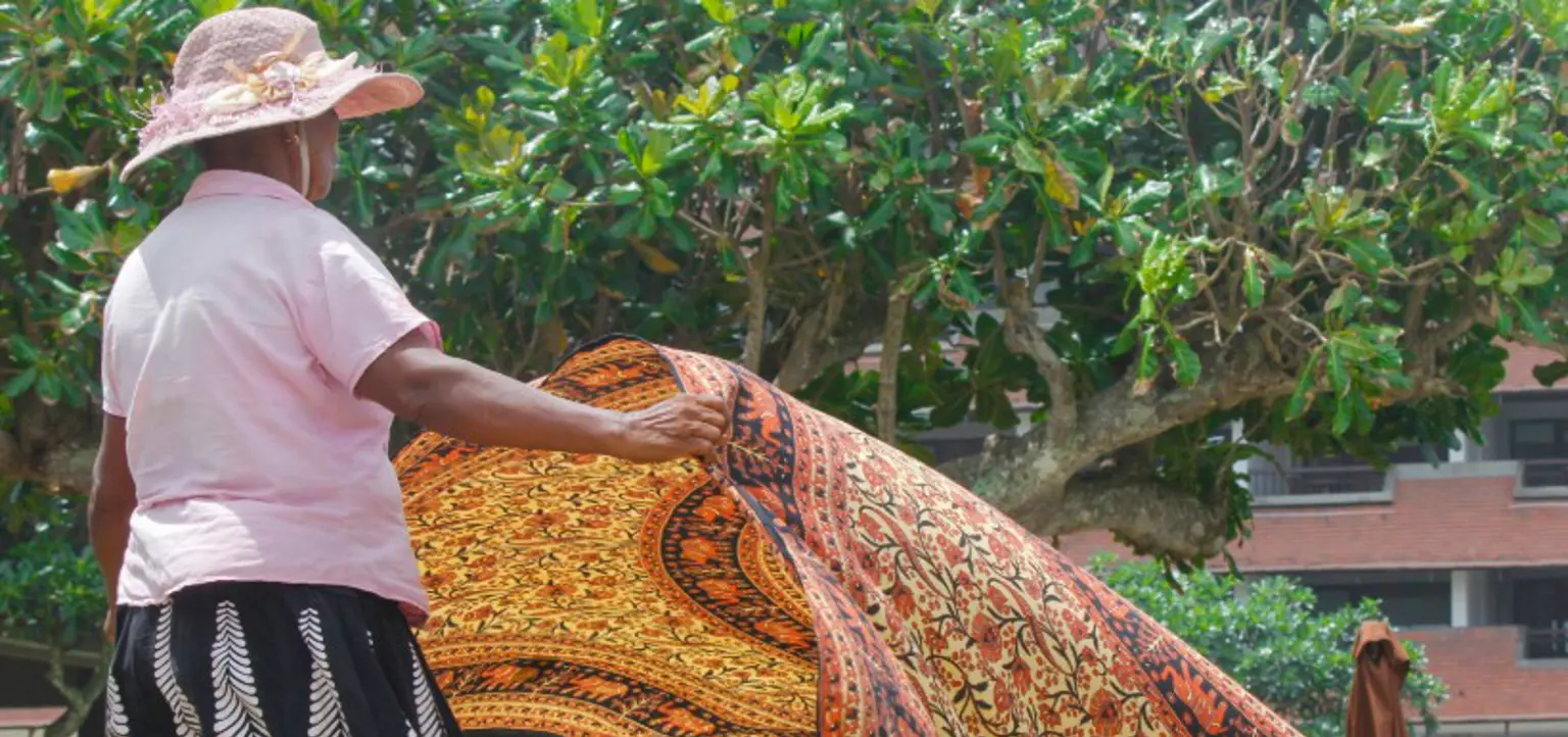 A Sri Lankan woman folding out a colorful tapestry.