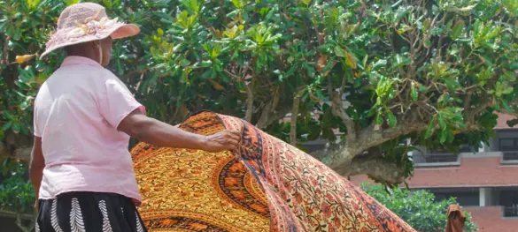 A Sri Lankan woman folding out a colorful tapestry.