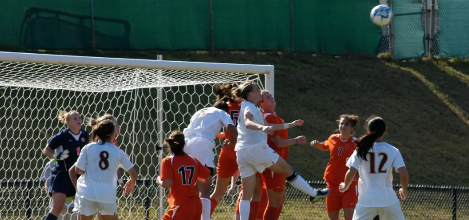 A women's soccer match with a group of players jumping to head the ball