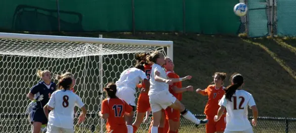A women's soccer match with a group of players jumping to head the ball