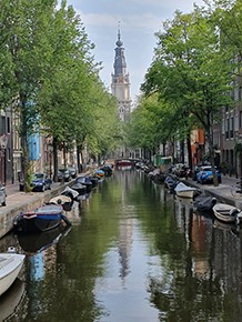 Photograph of the view of a canal in Amsterdam, Netherlands, lined with moored boats and traditional Dutch buildings, taken in 2019.