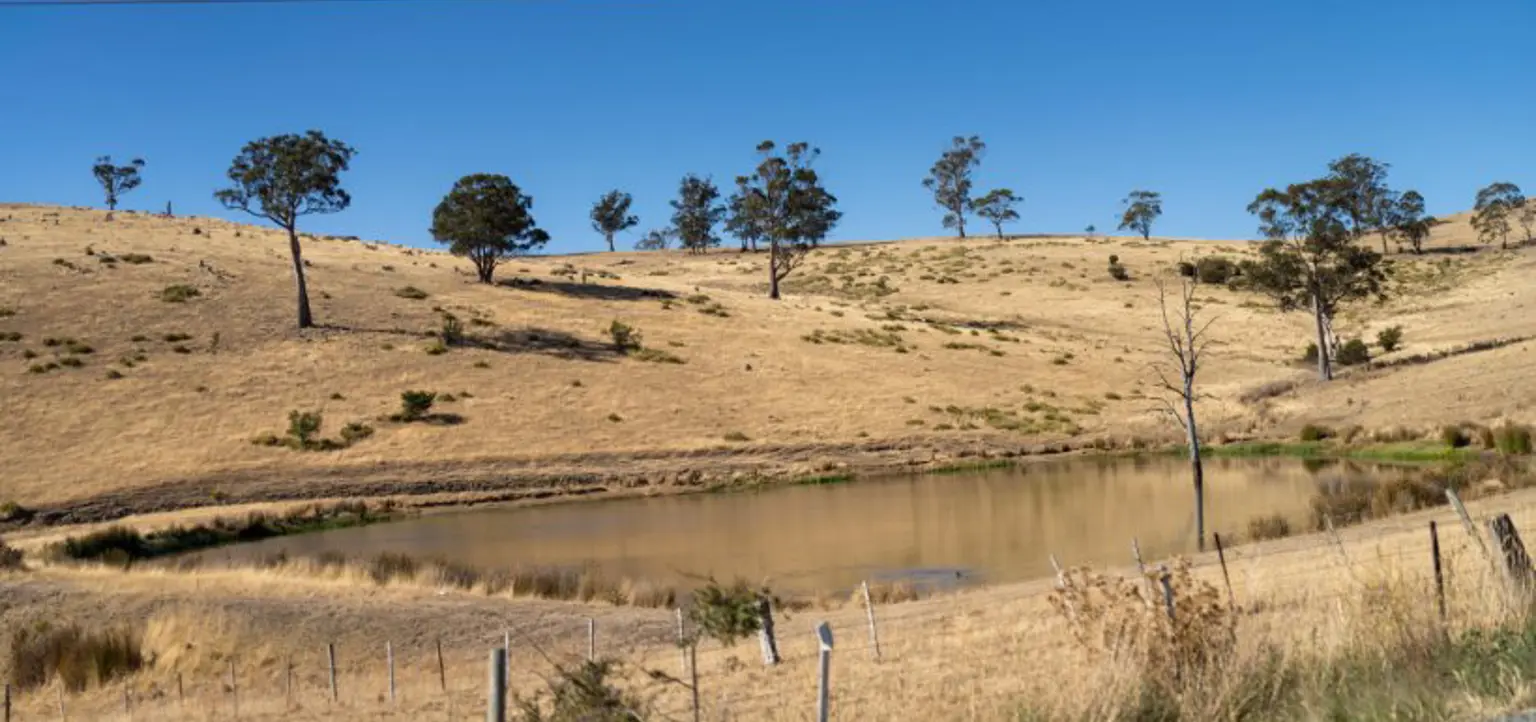 A dam in a drying landscape, with a farm fence in the foreground