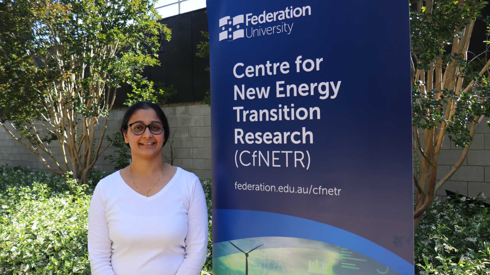 A female wearing a white top standing beside a sign that has Centre for New Energy Transition Research (CfNERT)
