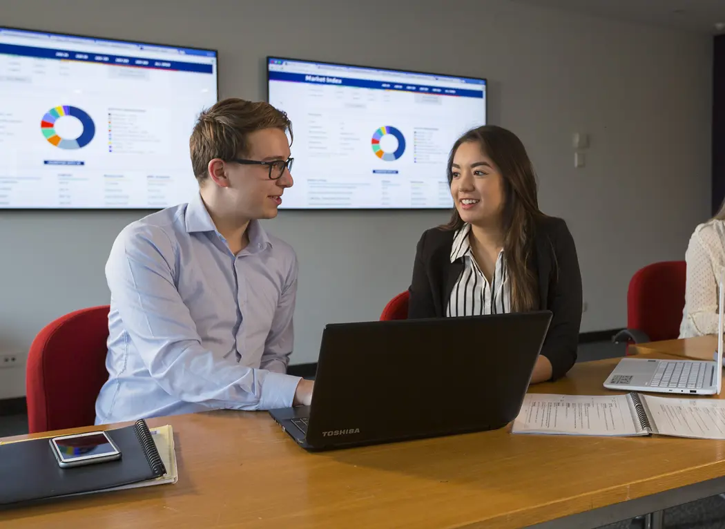 Two people sit in a work meeting with a laptop open