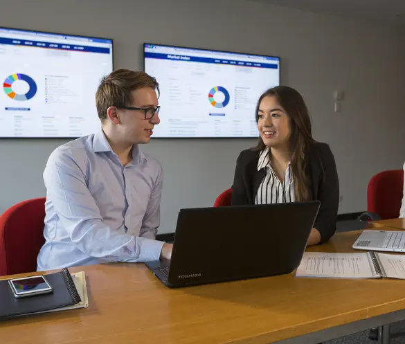 Two people sit in a work meeting with a laptop open