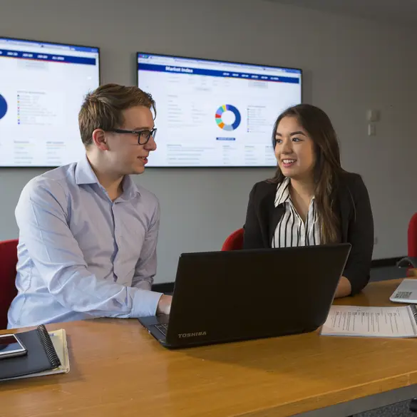 Two people sit in a work meeting with a laptop open