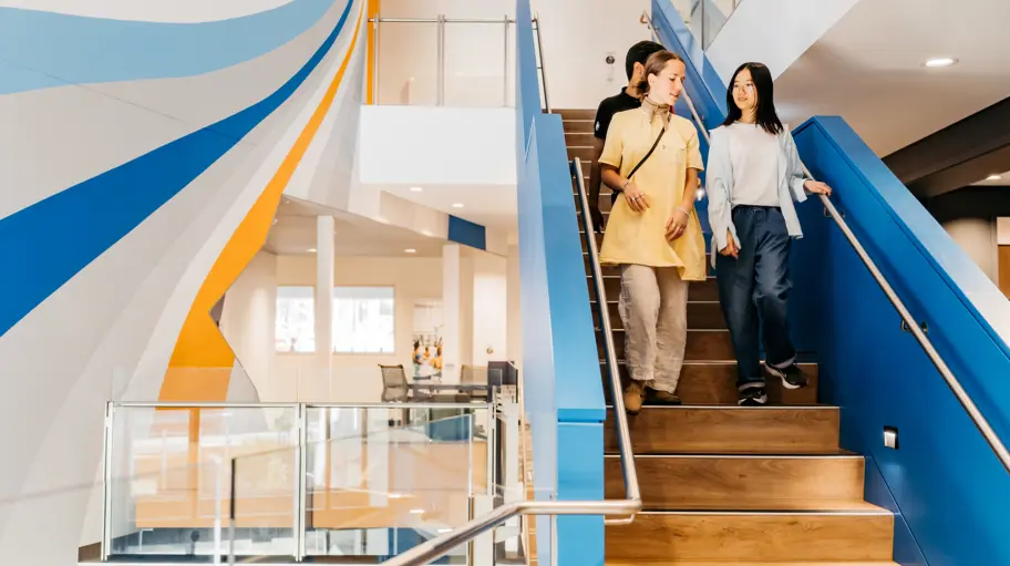 Photo of 3 people walking down a staircase in a modern looking building.